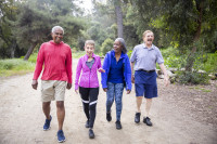 4 older people, two women and two men, are walking on a trail in the forest