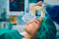 an Asian woman lies on an operating table and a physician puts a breathing mask over her face