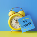 Alarm clock and a blue post it note that says 'Quit Smoking' with  a blue background 