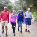 4 older people, two women and two men, are walking on a trail in the forest
