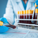 A researcher wearing gloves and a white coat holds up tubes of blood for testing