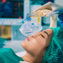 an Asian woman lies on an operating table and a physician puts a breathing mask over her face