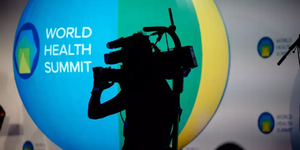 Man with camera in front of World Health Summit logo