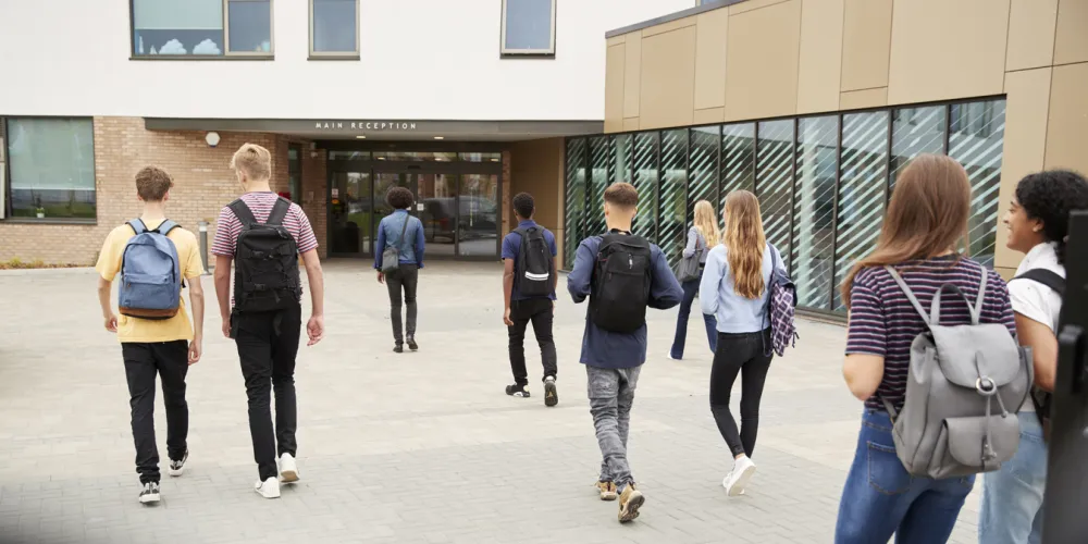 Rear View Of High School Students Walking Into College Building Together