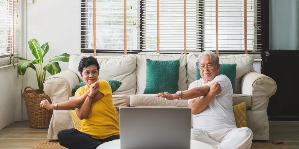 Two older adults stretch whilst following a virtual exercise-based cardiac rehabilitation session