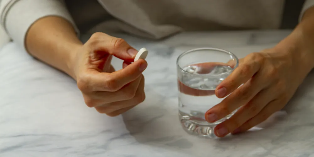 Hands holding a white tablet above a glass of water