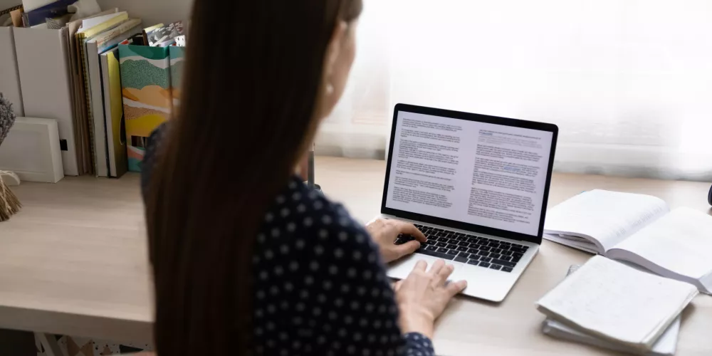 Back view of young lady working from home focused on computer screen 