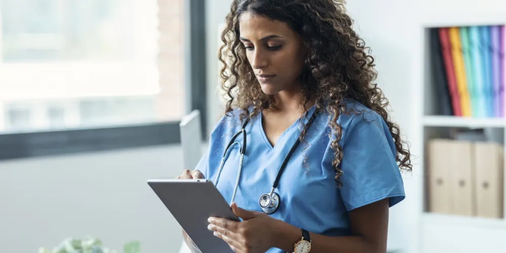 Shot of female healthcare professional using her digital tablet while standing in the consultation.