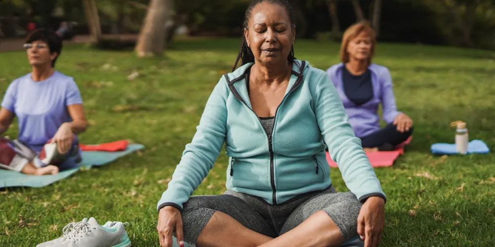 Older person meditates in park as part as a group