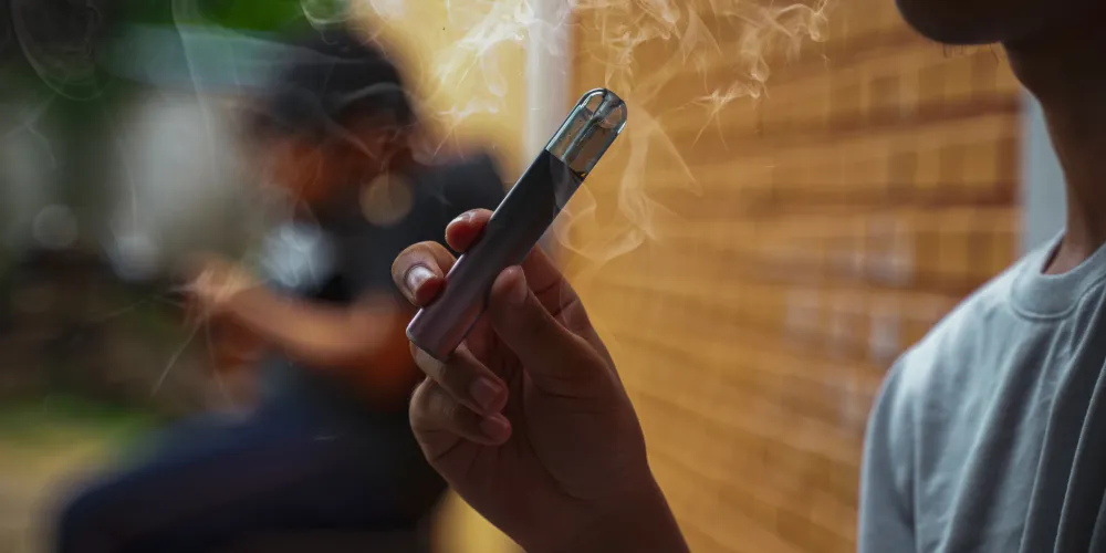 A person holds a vape. There is smoke in the air. 
