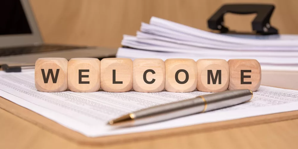 The word "welcome" is displayed with decorative wooden blocks in a professional office setting