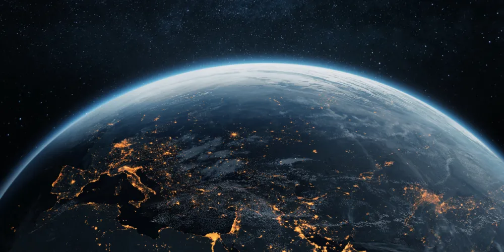 View of Earth from space at night, showing glowing city lights across Europe, the Middle East, and Asia. Planet Earth illuminated under a starry sky.