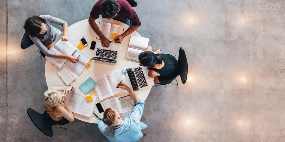Group of young students in cooperation with their academic assignment. Top view shot of young people studying together around a table.