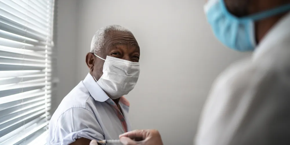 doctor administering a vaccine to an older man, both are wearing facemasks
