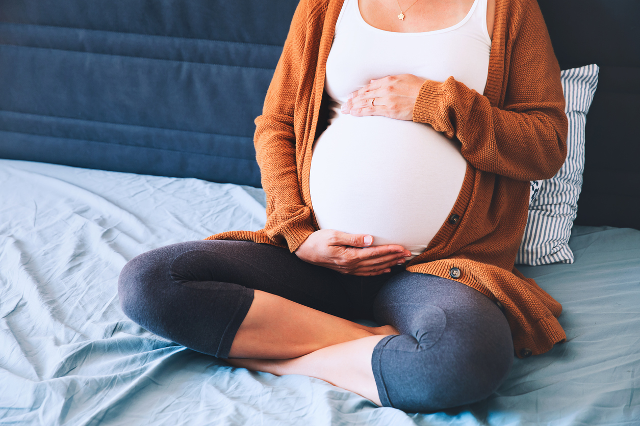 Pregnant woman sitting on a bed and holding her stomach